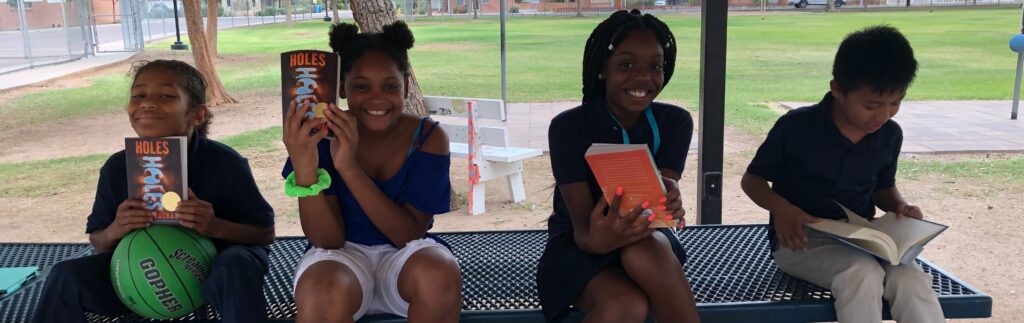 four students smile at the camera holding books